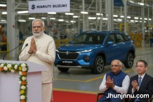 प्रधानमंत्री नरेंद्र मोदी गुजरात के हंसलपुर प्लांट में मारुति सुजुकी की पहली इलेक्ट्रिक SUV e-Vitara का शुभारंभ करते हुए, पृष्ठभूमि में EV कार और फैक्ट्री का दृश्य।